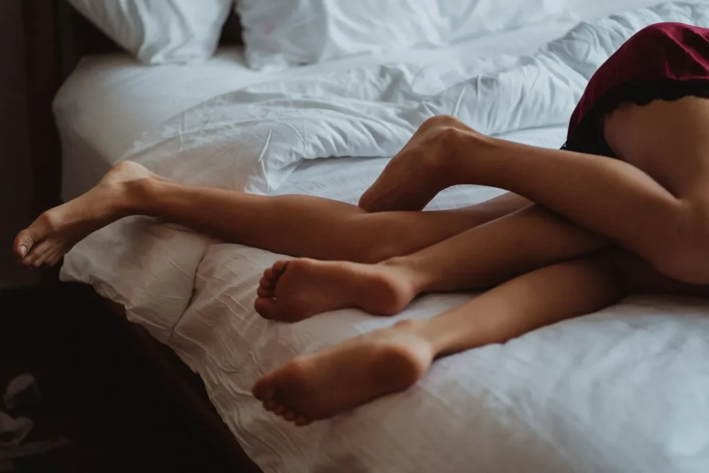 Un primer plano de piernas entrelazadas que ilustran intimidad y relajación en una cama para representar el concepto de ideas eróticas básicas.